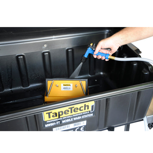 Close-up of a person using a TapeTech water sprayer to clean a finishing box inside a black wash basin