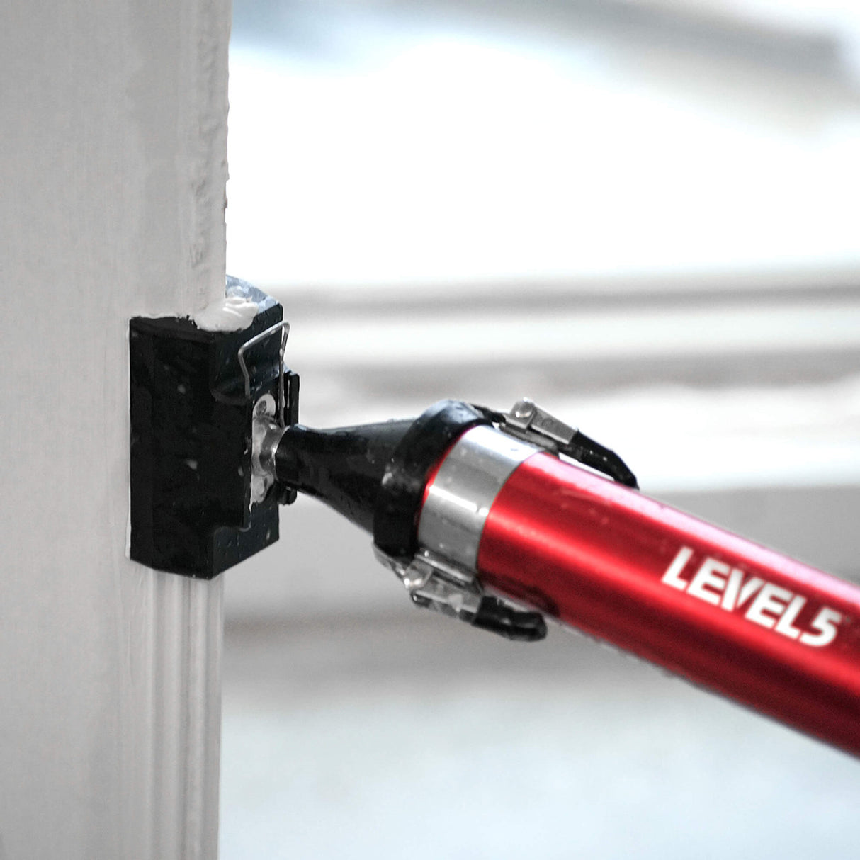 Close-up of red Level 5 Compound Applicator Tube with black outside corner applicator attachment applying mud to an outside corner