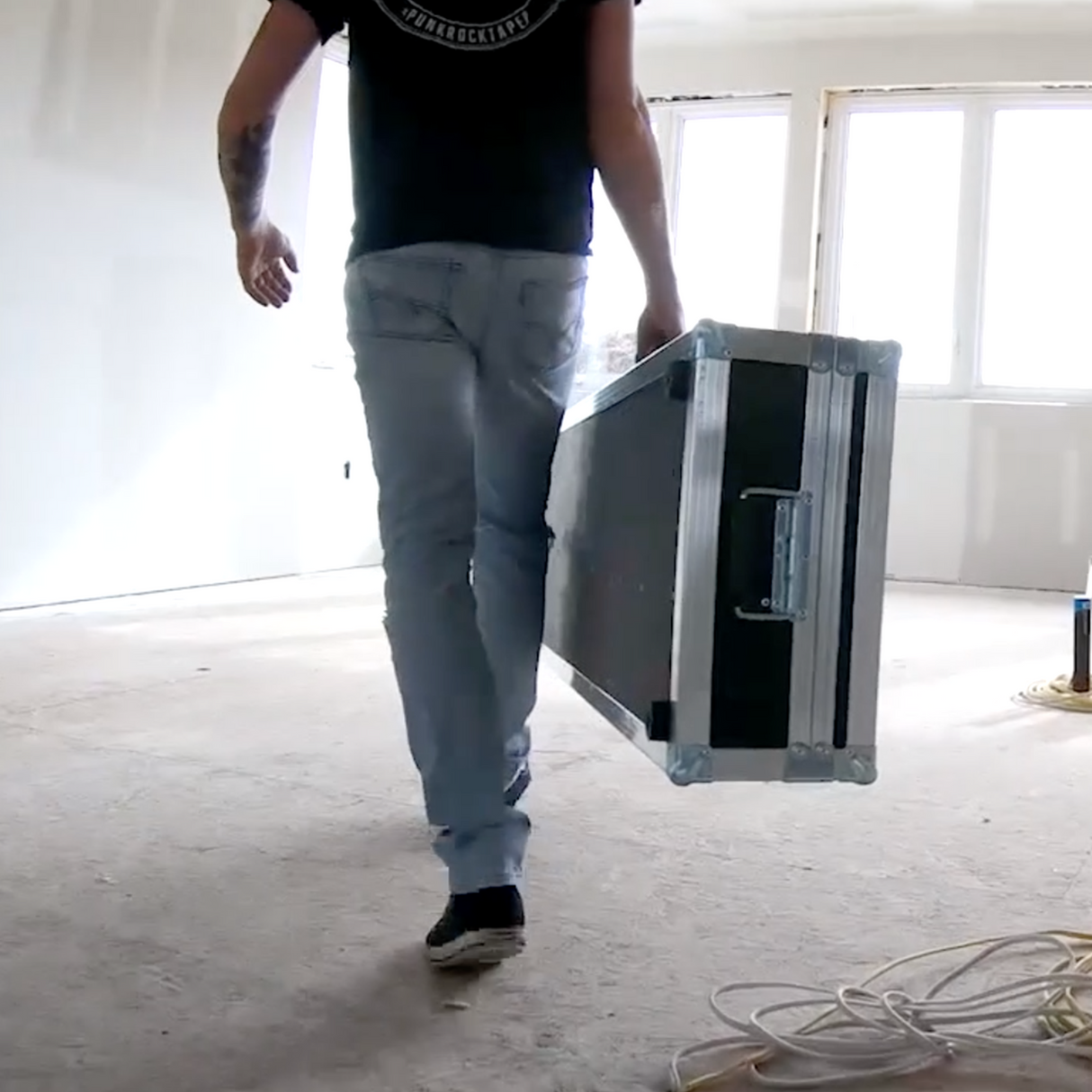 Person walking through job site holding a large black Columbia automatic taping tool case with rubber feet and rolling wheels