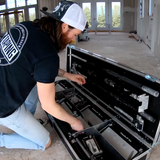 Man kneeling on the floor taking flat finishing boxes out of a large black open tool case at a job site