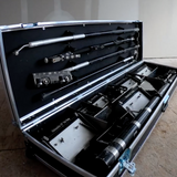 Close-up of an open black automatic tool case containing box handles, corner rollers, Fat Boy boxes, and an automatic taper on the floor at a job site